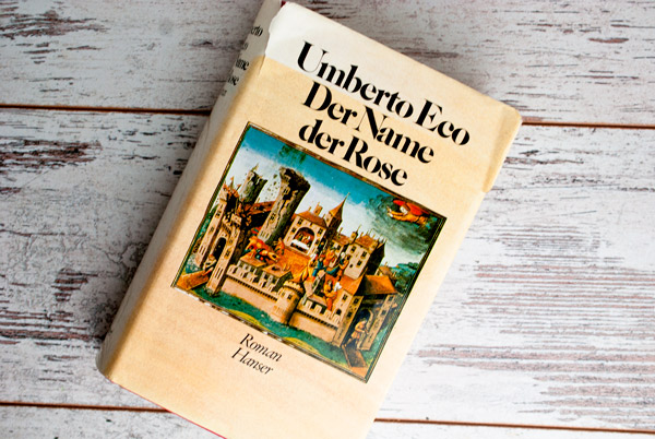Der Name der Rose von Umberto Eco, Buch liegend auf weißem Holzuntergrund