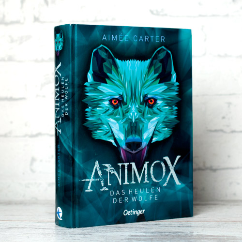 Buch "Animox Das Heulen der Wölfe" fotografiert vor weißem Hintergrund. Das Cover in Grüntönen zeigt einen Wolfskopf.