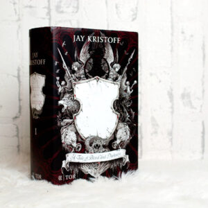 Jay Kristoff Das Reich der Vampire: Buch vor weißem Hintergrund fotografiert. Das Cover zeigt ein Wappen oder Schild vor dunkelrotem Hintergrund.